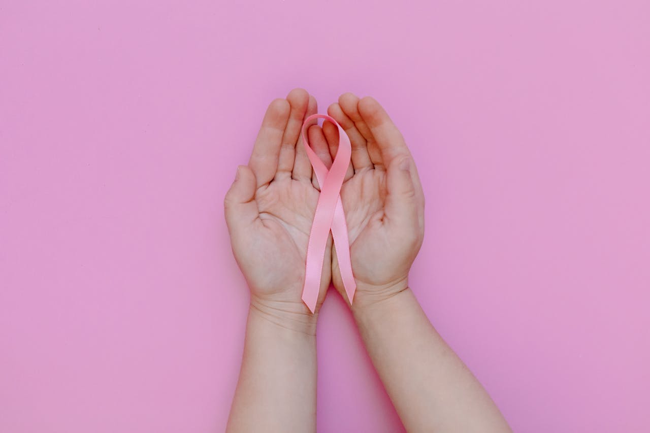 Childs hands holding pink ribbon for breast cancer awareness on pink background.